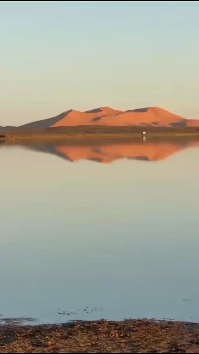 Un tramonto incantevole sul lago nel deserto di Merzouga, con acque calme che riflettono i colori caldi del cielo e le dune dorate che lo circondano.

@marocco.tours